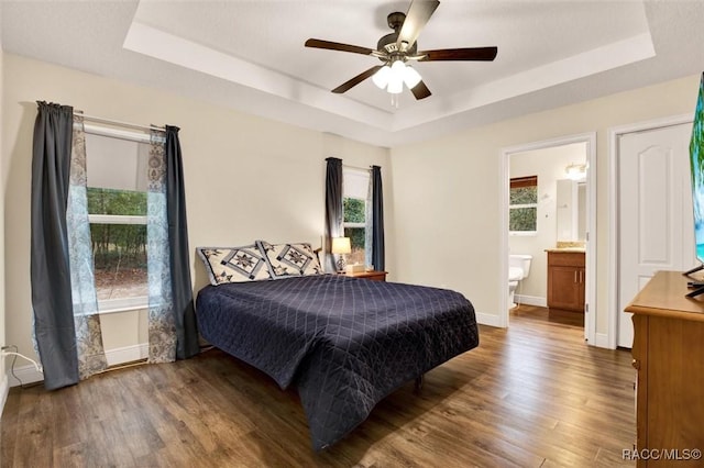 bedroom featuring dark wood-style floors, a tray ceiling, and multiple windows