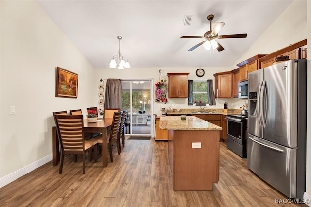 kitchen featuring lofted ceiling, appliances with stainless steel finishes, brown cabinets, a center island, and hanging light fixtures