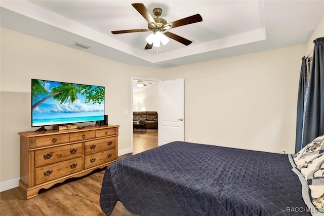 bedroom with baseboards, visible vents, a raised ceiling, ceiling fan, and wood finished floors