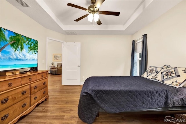 bedroom with light wood-style floors, visible vents, a tray ceiling, and ceiling fan