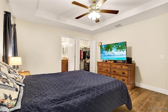 bedroom featuring baseboards, visible vents, a ceiling fan, wood finished floors, and a tray ceiling