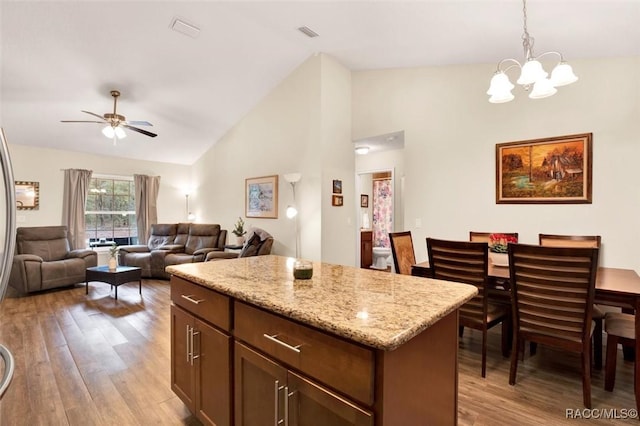 kitchen featuring light wood finished floors, hanging light fixtures, open floor plan, a kitchen island, and light stone countertops