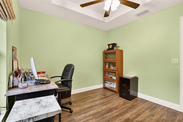 office space with a raised ceiling, visible vents, baseboards, and wood finished floors