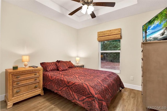 bedroom with light wood-style floors, baseboards, a tray ceiling, and ceiling fan