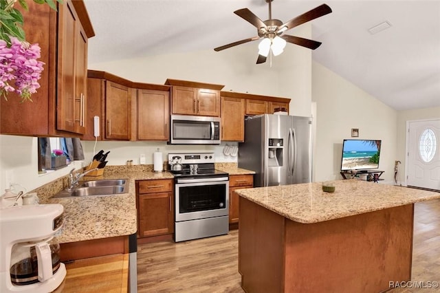 kitchen featuring lofted ceiling, appliances with stainless steel finishes, light wood-style floors, brown cabinetry, and a sink