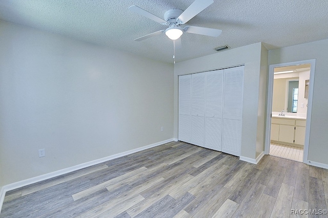 unfurnished bedroom featuring sink, ceiling fan, a textured ceiling, light hardwood / wood-style floors, and a closet