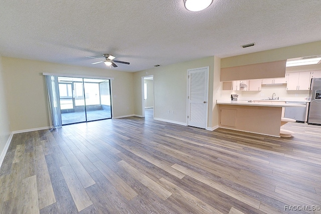 unfurnished living room with ceiling fan, a textured ceiling, and light wood-type flooring