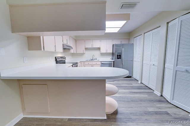 kitchen featuring a breakfast bar, sink, light wood-type flooring, appliances with stainless steel finishes, and kitchen peninsula