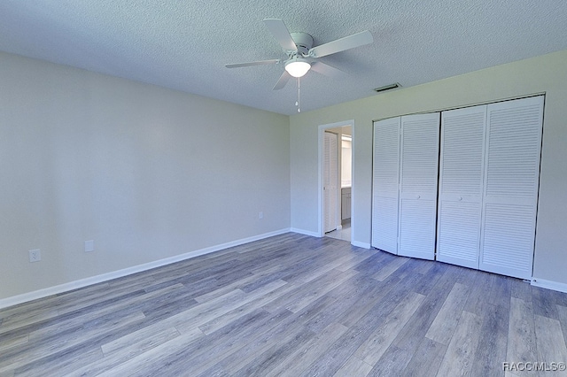 unfurnished bedroom featuring a textured ceiling, a closet, hardwood / wood-style flooring, and ceiling fan