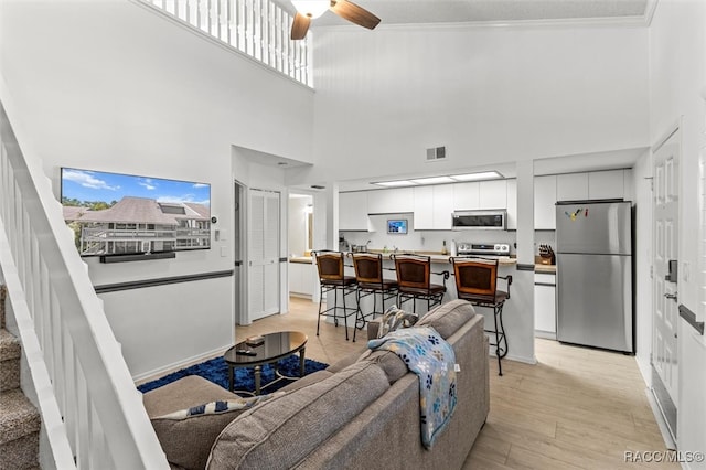 living room with a high ceiling, light hardwood / wood-style floors, ceiling fan, and crown molding