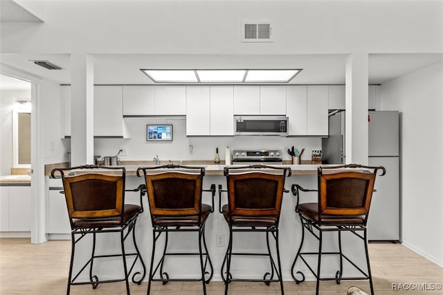 kitchen with white cabinets, a kitchen bar, appliances with stainless steel finishes, and light hardwood / wood-style flooring