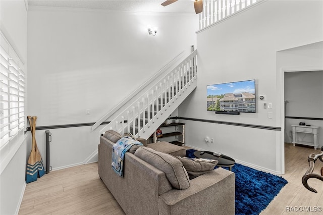 living room featuring a high ceiling, light hardwood / wood-style flooring, ceiling fan, and crown molding