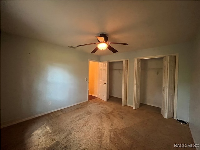 unfurnished bedroom with ceiling fan, two closets, and carpet floors