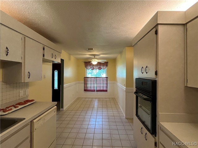 kitchen featuring a textured ceiling, black oven, ceiling fan, light tile patterned flooring, and white dishwasher