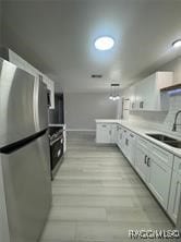 kitchen featuring stainless steel refrigerator, sink, and white cabinets