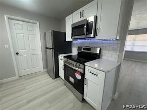 kitchen featuring backsplash, white cabinetry, stainless steel appliances, and light wood-type flooring