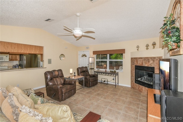 tiled living room featuring ceiling fan, a tiled fireplace, a textured ceiling, and vaulted ceiling