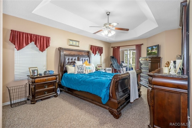 carpeted bedroom featuring ceiling fan, access to exterior, and a tray ceiling