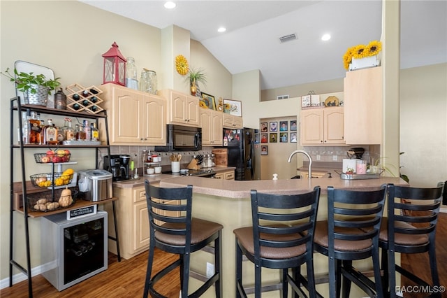 kitchen with kitchen peninsula, tasteful backsplash, vaulted ceiling, black appliances, and dark hardwood / wood-style floors