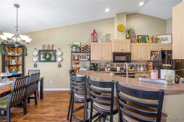 kitchen featuring tasteful backsplash, a notable chandelier, lofted ceiling, black appliances, and hardwood / wood-style flooring