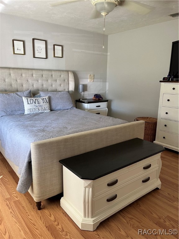 bedroom with a textured ceiling, light hardwood / wood-style flooring, and ceiling fan