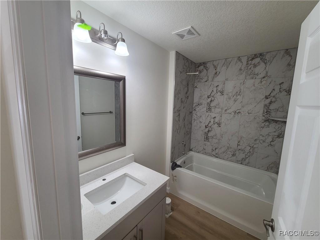 37 N Independence Hwy, Inverness, FL 34453 - bathroom featuring a textured ceiling,  shower combination, visible vents, wood finished floors, and vanity