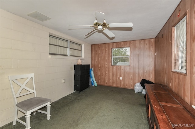 unfurnished room with dark carpet, ceiling fan, and wood walls