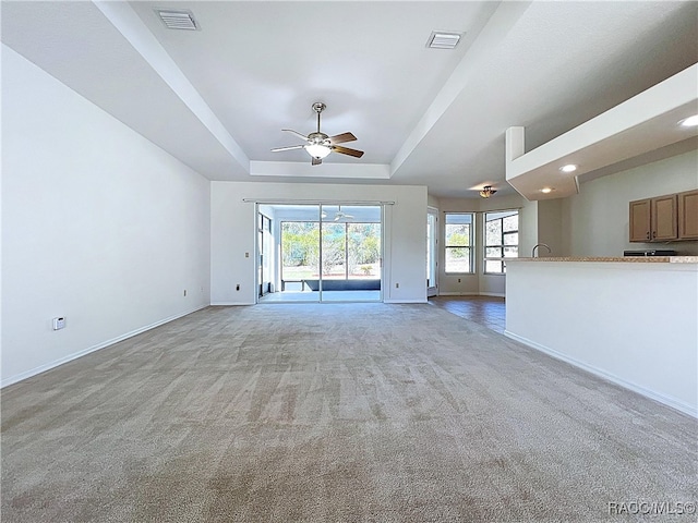 unfurnished living room featuring visible vents, a raised ceiling, baseboards, and a ceiling fan