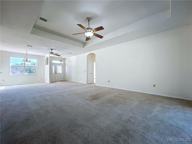 unfurnished living room with visible vents, baseboards, arched walkways, carpet, and a raised ceiling