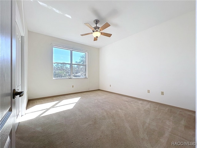 spare room featuring light carpet, a ceiling fan, and baseboards