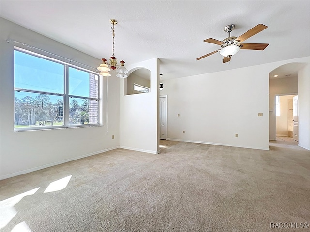 empty room with baseboards, arched walkways, light carpet, and ceiling fan with notable chandelier