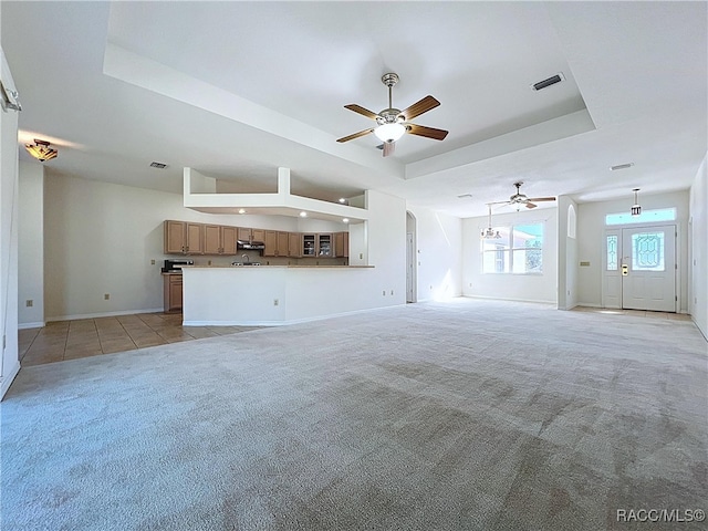 unfurnished living room featuring visible vents, a tray ceiling, arched walkways, baseboards, and light colored carpet