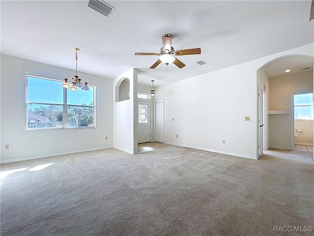 empty room with arched walkways, visible vents, light colored carpet, and baseboards