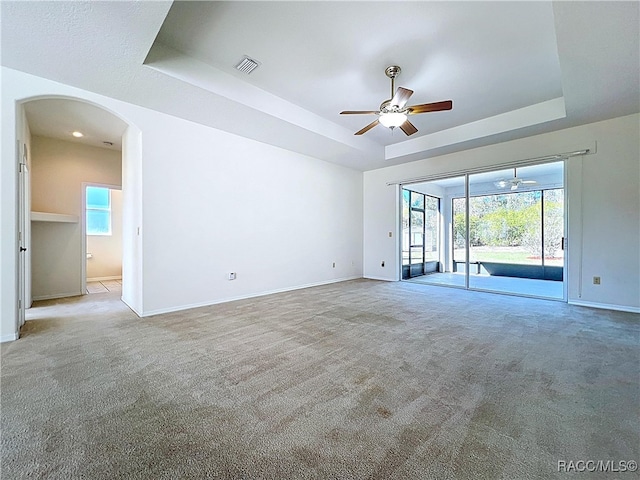 empty room with a tray ceiling, arched walkways, visible vents, and light carpet