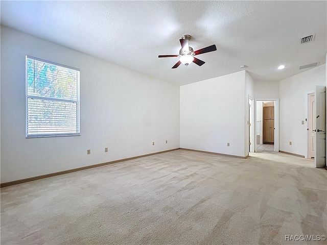 spare room featuring visible vents, light carpet, a textured ceiling, baseboards, and ceiling fan