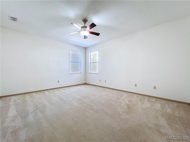 spare room with light colored carpet, visible vents, and a textured ceiling