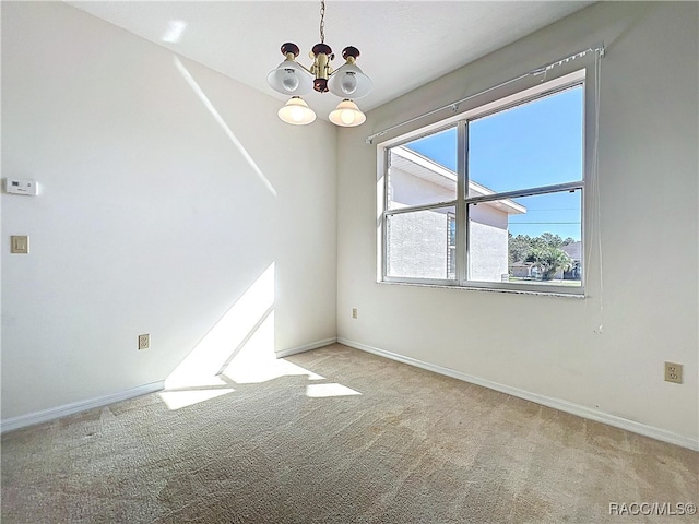 carpeted empty room with a notable chandelier and baseboards