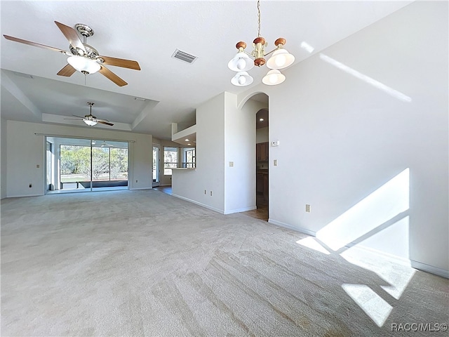 unfurnished living room featuring visible vents, baseboards, a tray ceiling, light carpet, and arched walkways