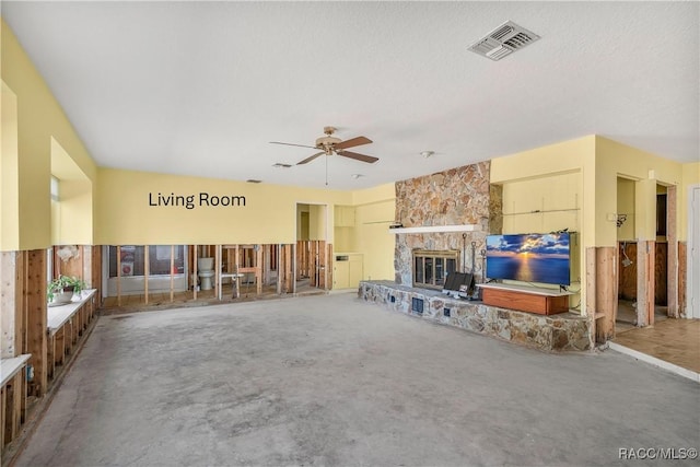 unfurnished living room with visible vents, a ceiling fan, a textured ceiling, a stone fireplace, and concrete floors