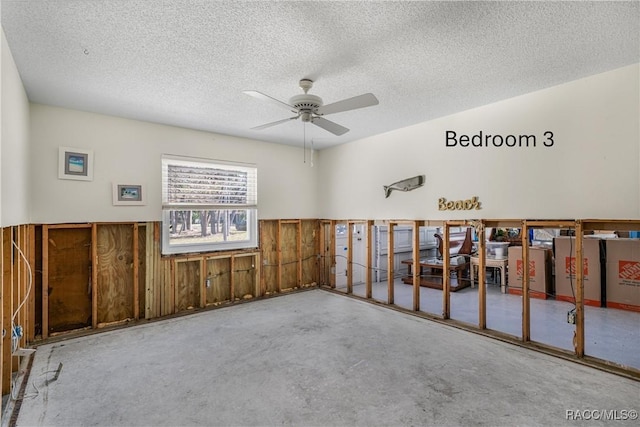 empty room featuring wainscoting, unfinished concrete flooring, wood walls, and a textured ceiling