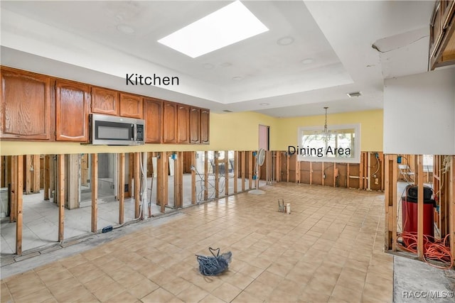 kitchen featuring a skylight, visible vents, stainless steel microwave, brown cabinets, and hanging light fixtures