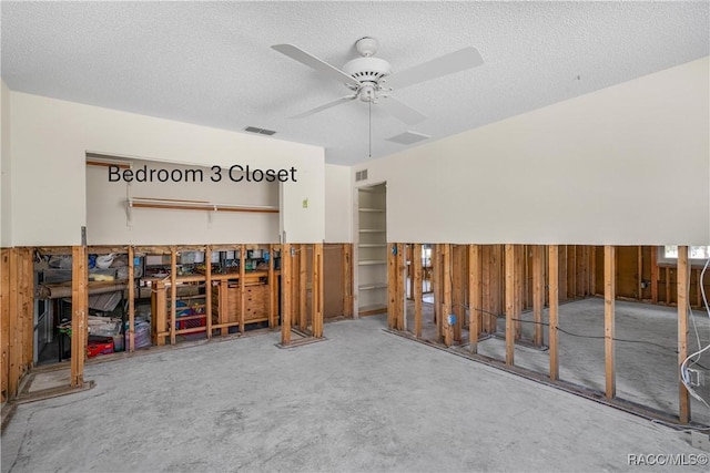 misc room with a textured ceiling, wood walls, visible vents, and a ceiling fan