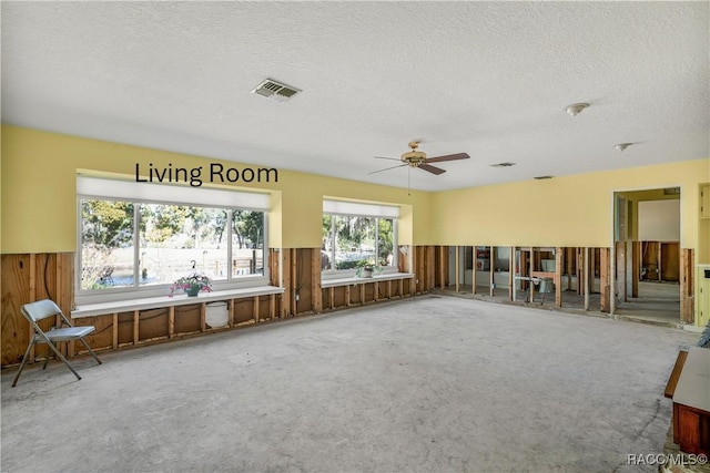 spare room featuring a textured ceiling, wooden walls, a ceiling fan, visible vents, and wainscoting