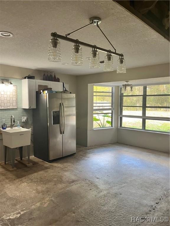 kitchen featuring sink, tasteful backsplash, stainless steel fridge with ice dispenser, concrete flooring, and white cabinets