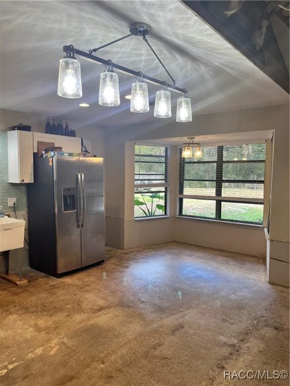 kitchen featuring white cabinetry, hanging light fixtures, tasteful backsplash, stainless steel fridge, and concrete flooring