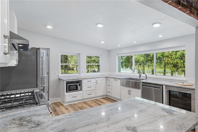 kitchen with light stone countertops, appliances with stainless steel finishes, sink, white cabinetry, and wine cooler