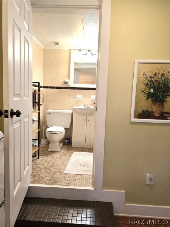 bathroom featuring tile patterned flooring, vanity, toilet, and tile walls