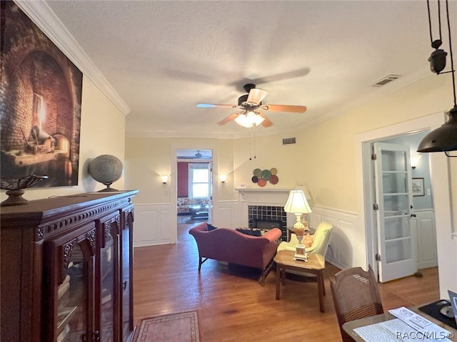 living room with a tiled fireplace, ceiling fan, hardwood / wood-style floors, and ornamental molding