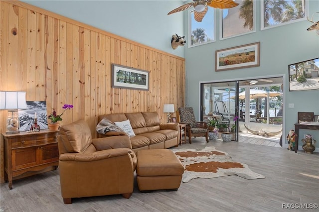 living room featuring ceiling fan, light hardwood / wood-style flooring, a towering ceiling, and wood walls