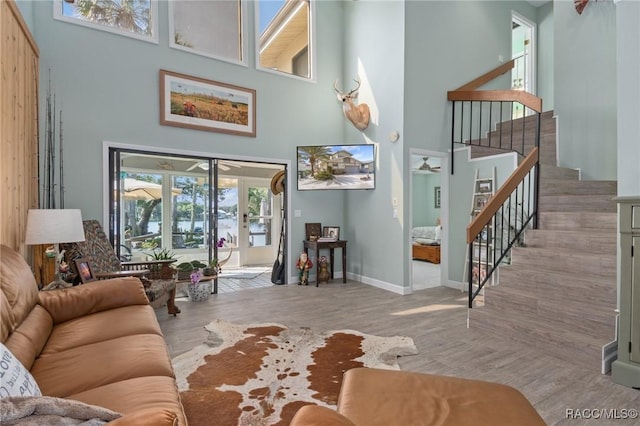 living room featuring ceiling fan, light wood-type flooring, a high ceiling, and french doors